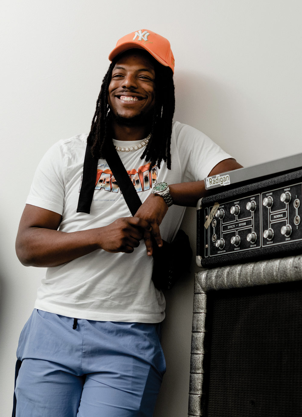 Student in orange yankees hat, smiling and leaning against guitar amp