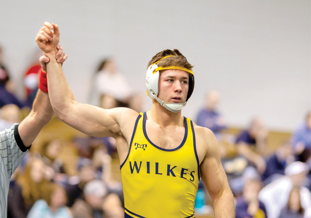Wilkes student wrestler having just won a match with hand being held up by referee